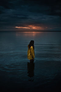 Woman standing on sea against sky during sunset