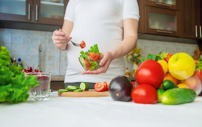 Midsection of pregnant woman with bowl of vegetables