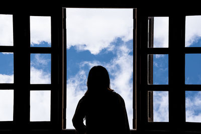 Rear view of silhouette man looking through window