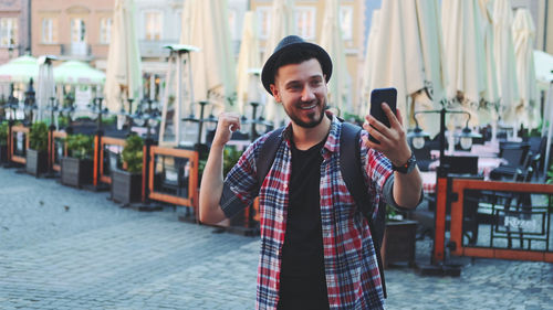 Portrait of smiling young man holding smart phone while standing outdoors