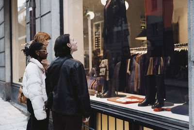 Multiracial female friends doing window shopping while standing at street