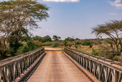 Footbridge along plants and trees against sky