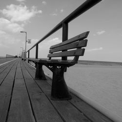 Empty bench on pier by sea against sky
