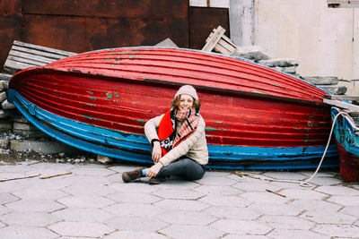 Portrait of woman smiling while sitting against red boat on footpath