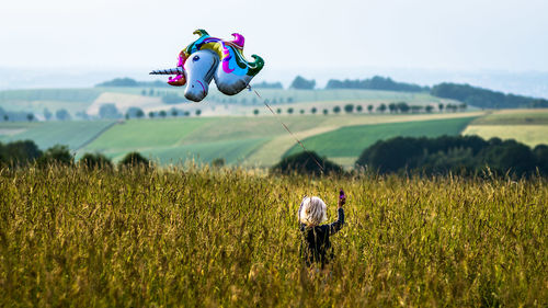 Rear view of girl holding balloon standing on field