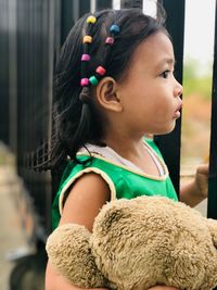 Side view of girl with teddy bear standing by fence