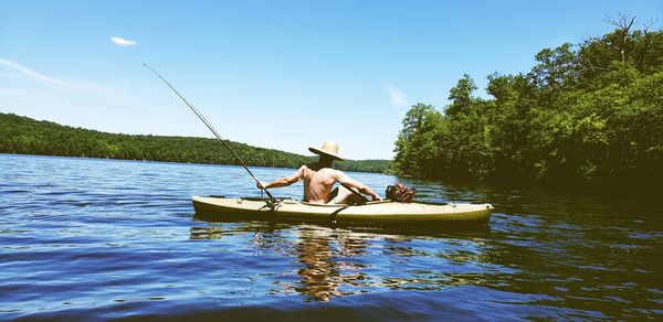 Rear view of shirtless man fishing in boat against sky