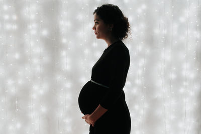 Side view of pregnant woman standing against illuminated wall