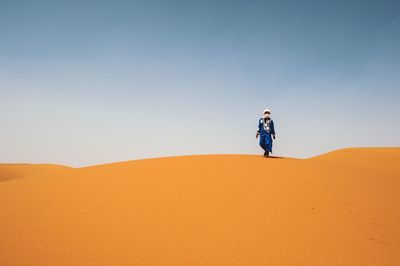 Man walking on sand dune in desert against clear sky