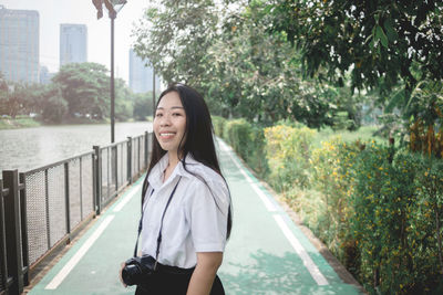 Portrait of smiling young woman standing on railing against trees