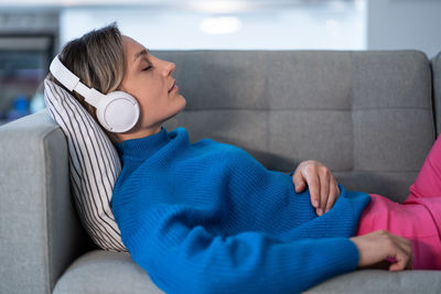 Young woman enjoying nice music in wireless headphones closes eyes and rests on comfortable sofa