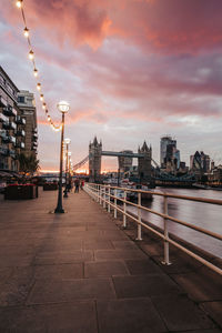 Illuminated bridge over river by buildings against sky during sunset