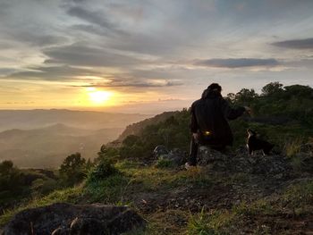 Rear view of man with puppy at mountain peak during sunset