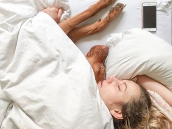 High angle view of woman sleeping with dog on bed at home