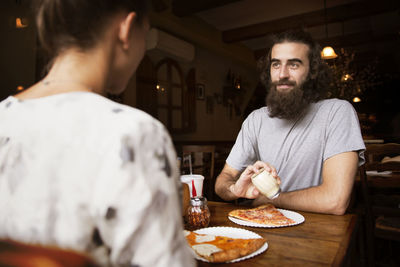 Midsection of friends having pizza at wooden table in restaurant