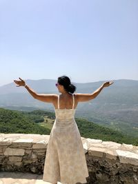 Rear view of woman with arms outstretched standing on mountain against sky