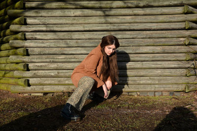 Young girl squats on the floor in front of old wooden planks, looks down