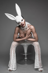 Portrait of young woman wearing rabbit costume against gray background