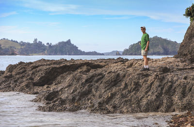 Man standing on rock by sea against sky