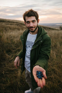 Portrait of smiling man holding berries on field