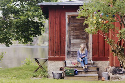 Smiling woman with organic vegetable sitting outside wooden cottage