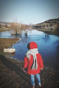 Rear view of girl standing by lake against clear sky