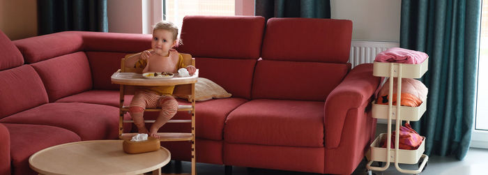 Banner toddler girl eating happily in high chair food by herself in the room. child having meal