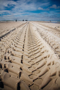 Surface level of tire tracks on sand at beach against sky