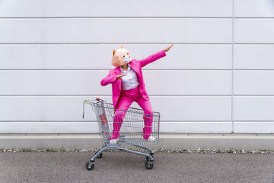 Full length of woman with pink umbrella against wall