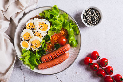 Fried sausages, tomatoes, lettuce and a sandwich with a boiled egg on a plate top view