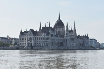 View of buildings by river against sky in city