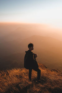 Man standing on cliff against sky during sunset