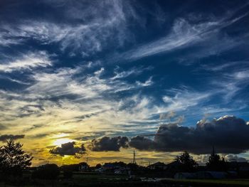 Silhouette of trees on landscape against dramatic sky