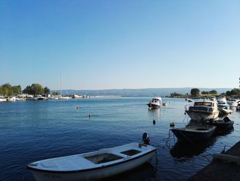 Boats moored at harbor against clear blue sky