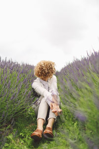 Woman sitting on lavender field against sky