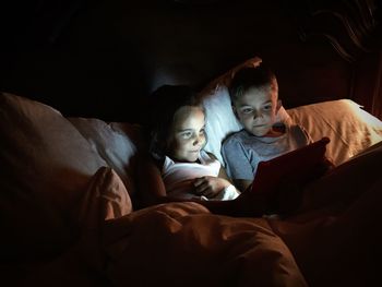 Smiling siblings using digital tablet on bed at home