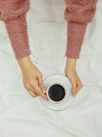 Cropped hands of woman holding coffee on bed