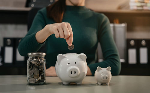 Midsection of woman putting coin in piggy bank