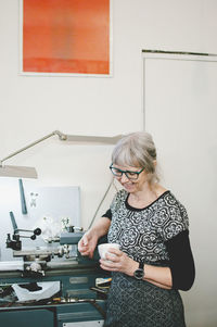 Senior woman smiling while holding coffee cup in jewelry workshop