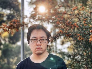 Portrait of young asian man standing against orange rowan berry trees.