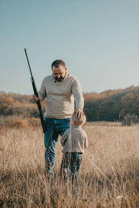 Full length of man holding camera on field against clear sky