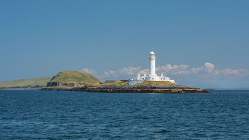 Lighthouse by sea against clear blue sky