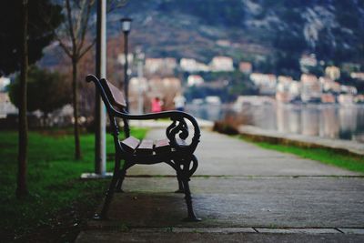 Empty bench in park against buildings in city