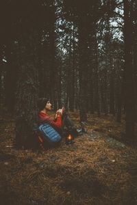 Man sitting on field by trees in forest