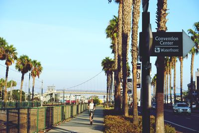 Close-up of road sign with man riding push scooter on footpath against sky in city