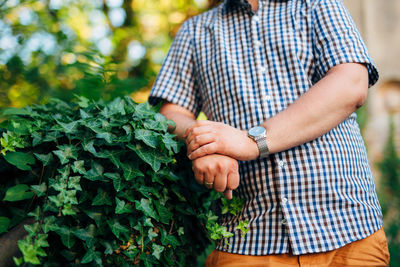 Midsection of man holding umbrella standing against plants