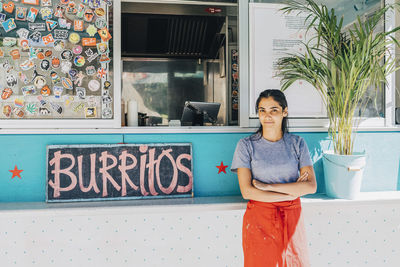Portrait of confident young female saleswoman standing with arms crossed against food truck