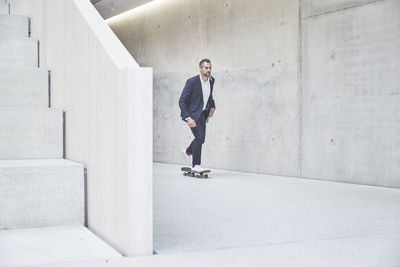 Businesssman riding skateboard along concrete wall