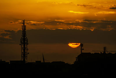 Silhouette communications tower and buildings against sky during sunset