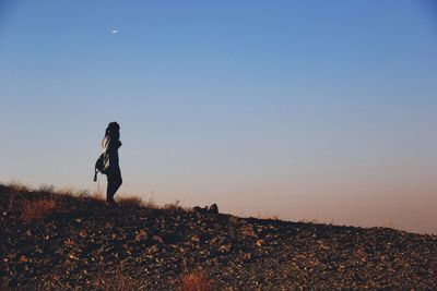 Side view of woman walking on mountain against clear sky during sunset